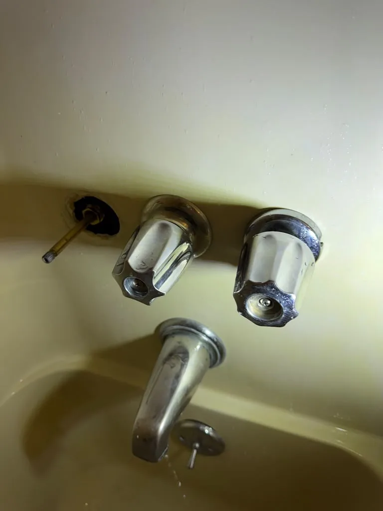 Old chrome bathtub faucet and handles with water running from the spout
